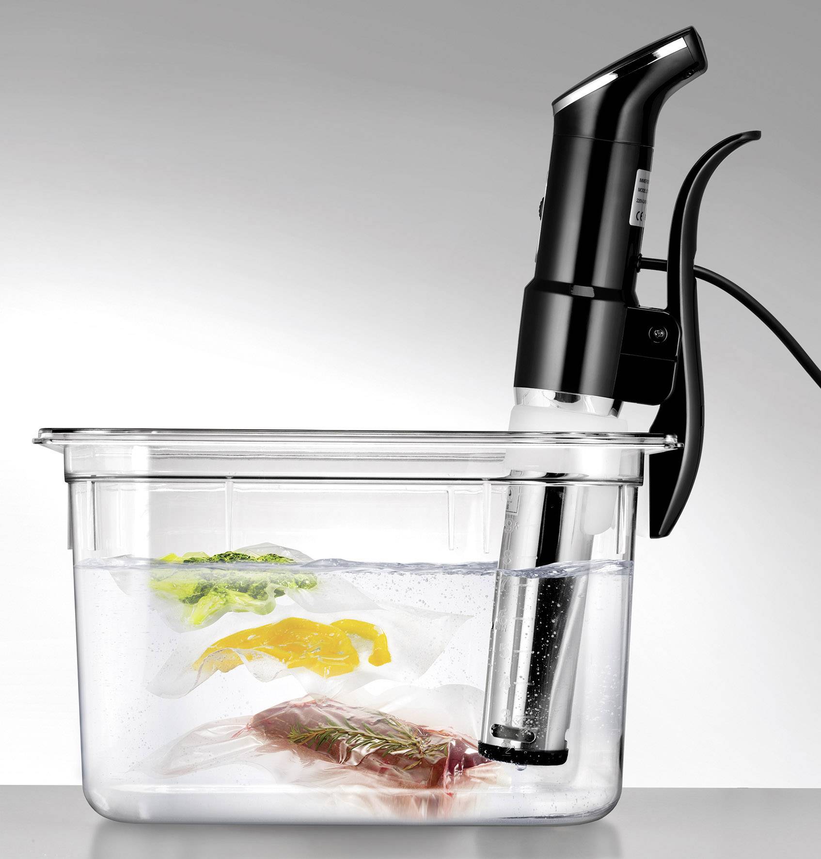 La machine sous-vide chauffe le bain-marie dans lequel des sachets sous vide contenant des légumes verts et jaunes ainsi que de la viande flottent.