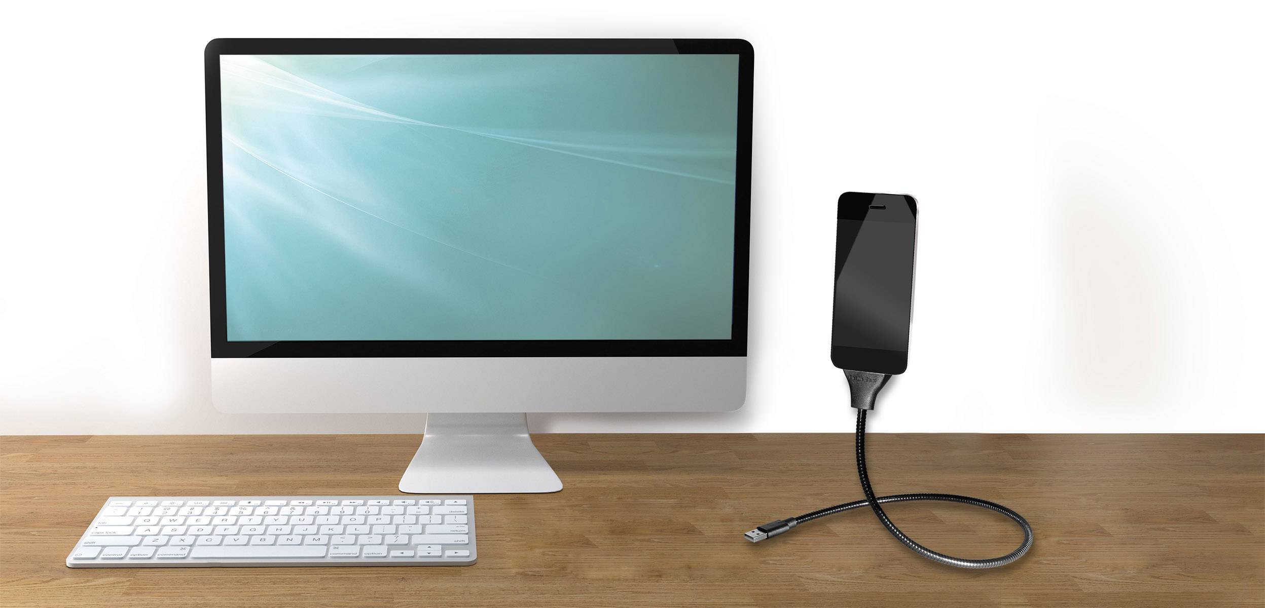 Un écran d'ordinateur et un clavier sur une table, reliés à un smartphone par un câble de charge.