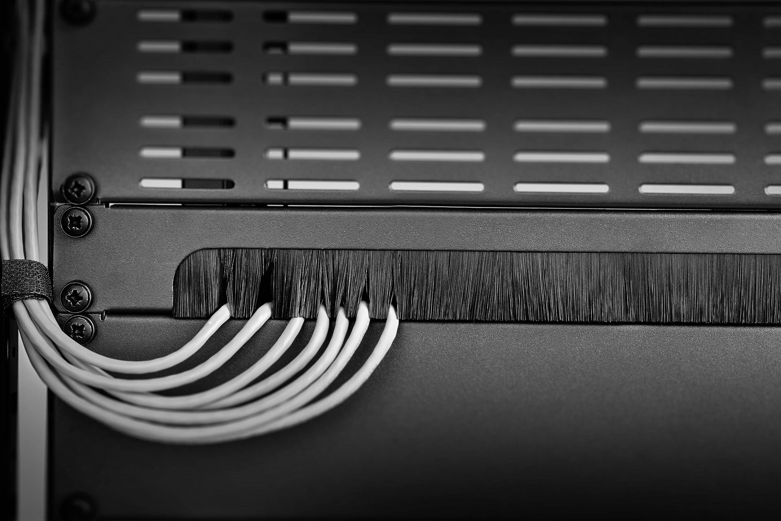 Plusieurs câbles blancs traversent une ouverture de brosse noire sur un boîtier électronique, ce qui témoigne d'une gestion de câbles soignée.