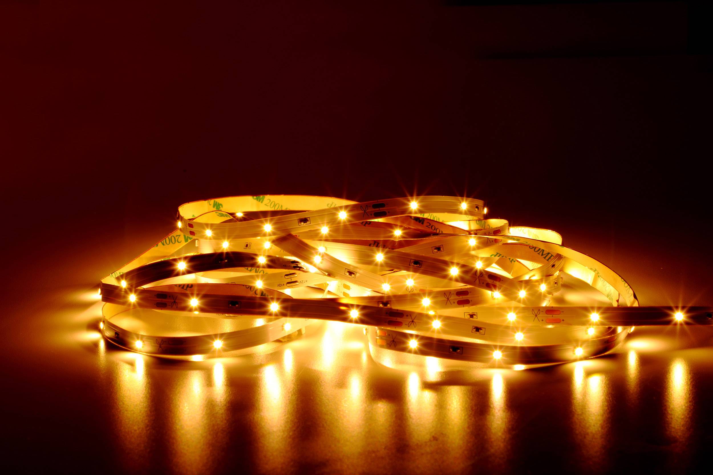 Bande de LED éclairée dans une lumière orange chaude sur une surface réfléchissante, créant une atmosphère chaleureuse et accueillante.