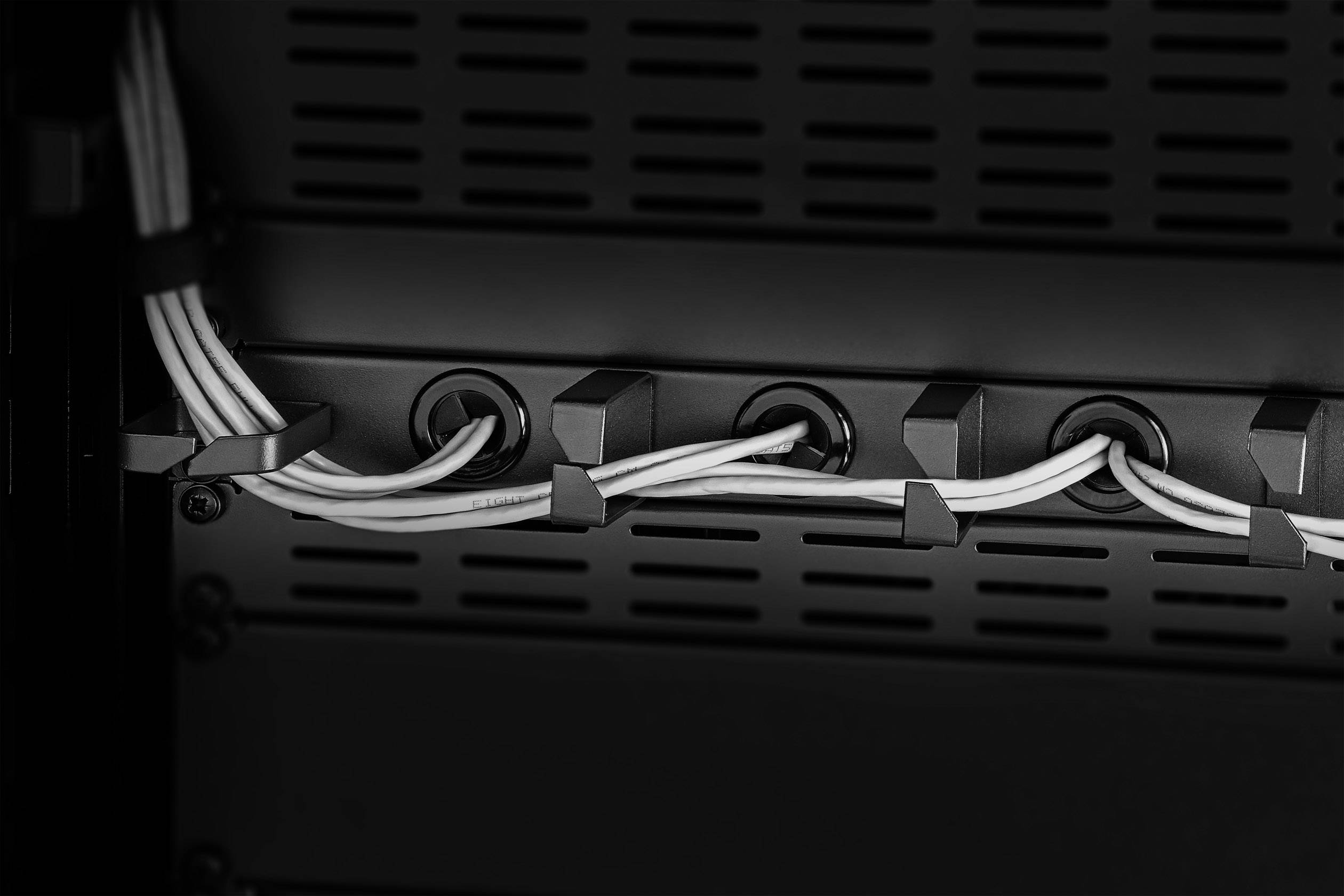 Plusieurs câbles blancs s'étendent parallèlement à travers un système de gestion de câbles noir dans un rack serveur ou réseau.