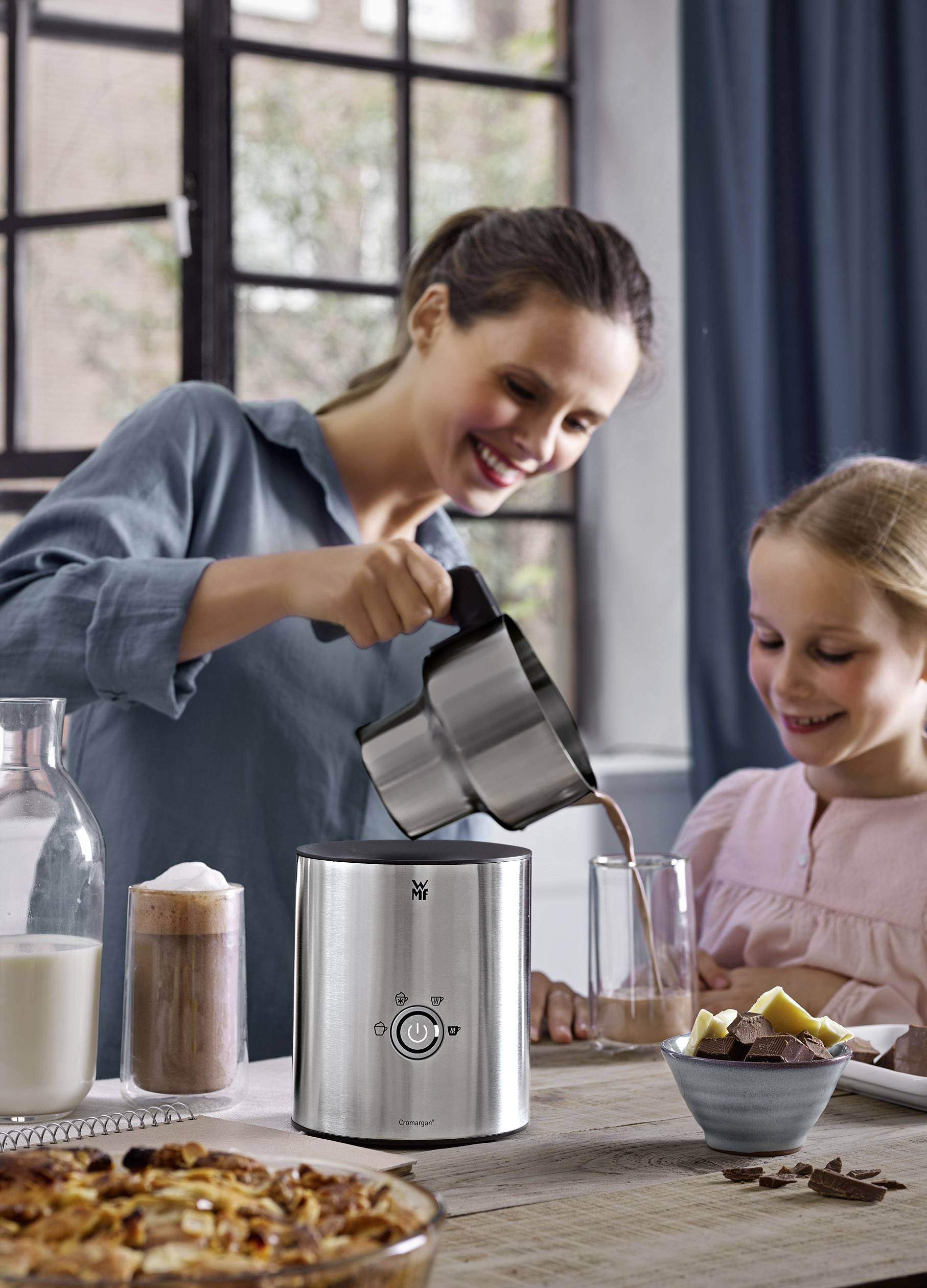 Une femme verse du chocolat chaud d'un mousseur à lait dans un verre, sous le regard d'une jeune fille. Vue sur une fenêtre en arrière-plan.