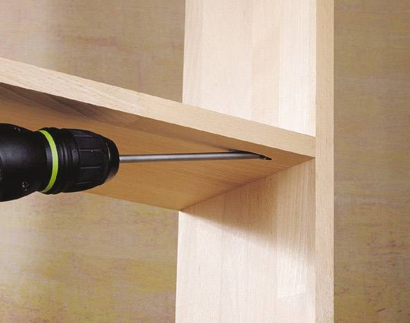 Une perceuse visse une étagère sur un poteau vertical en bois. L'étagère est faite de bois clair.