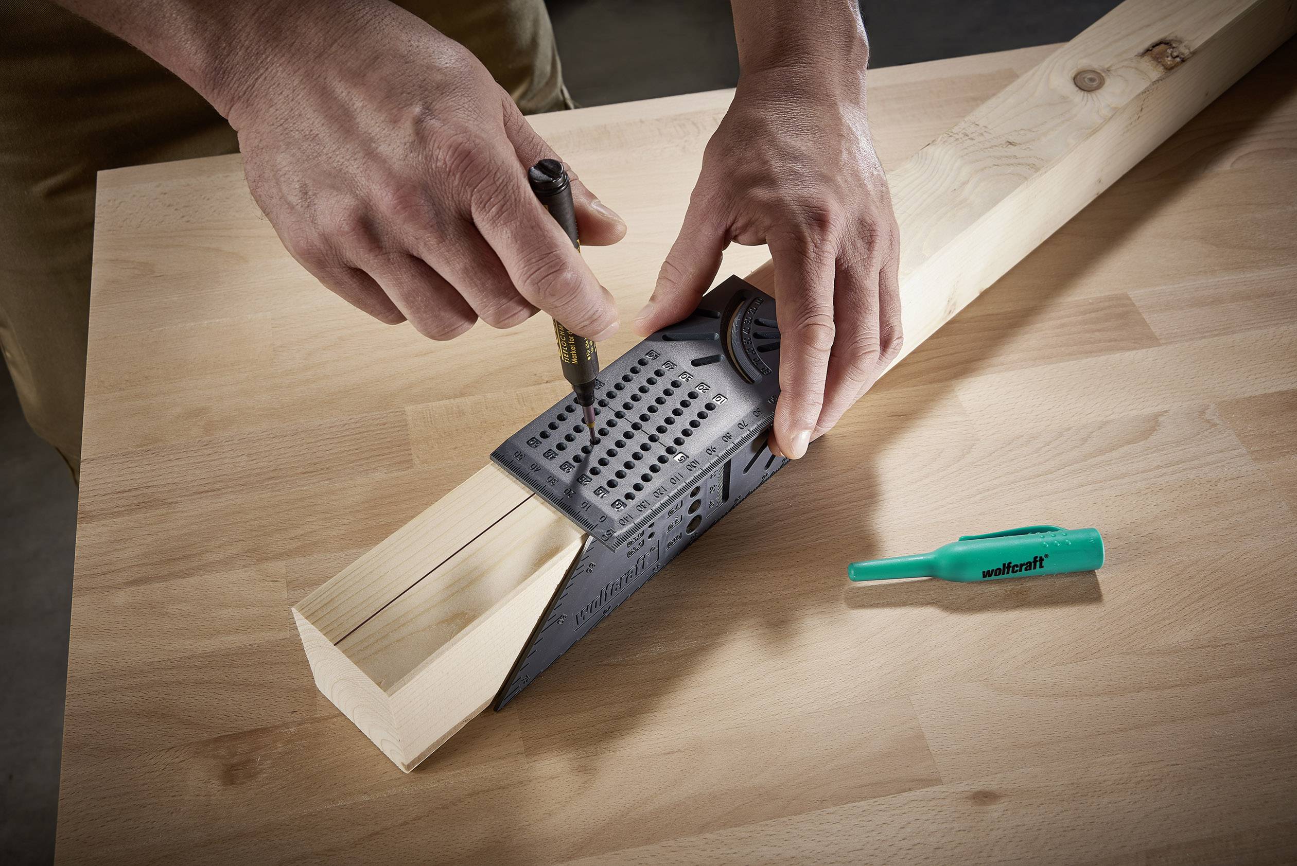 Une personne utilise un outil de mesure multifonctionnel pour effectuer des marquages précis sur un morceau de bois posé sur une table de travail.