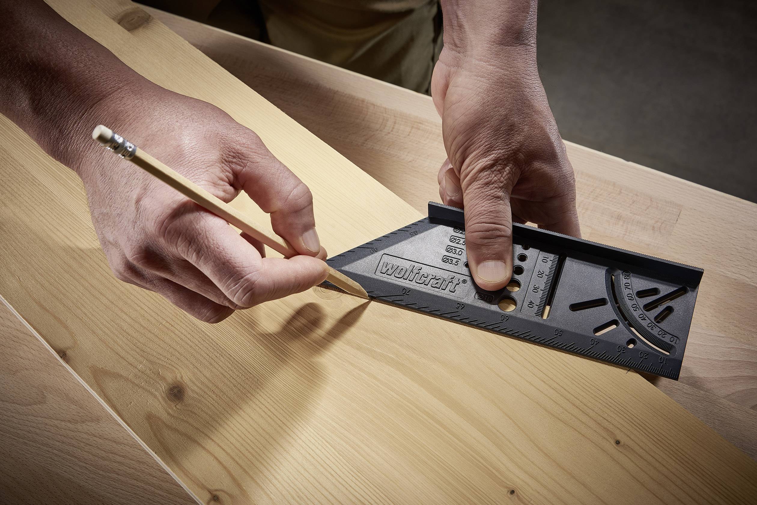 Une personne trace une ligne au crayon sur une planche de bois en utilisant un outil de mesure d'angle pour un alignement précis.