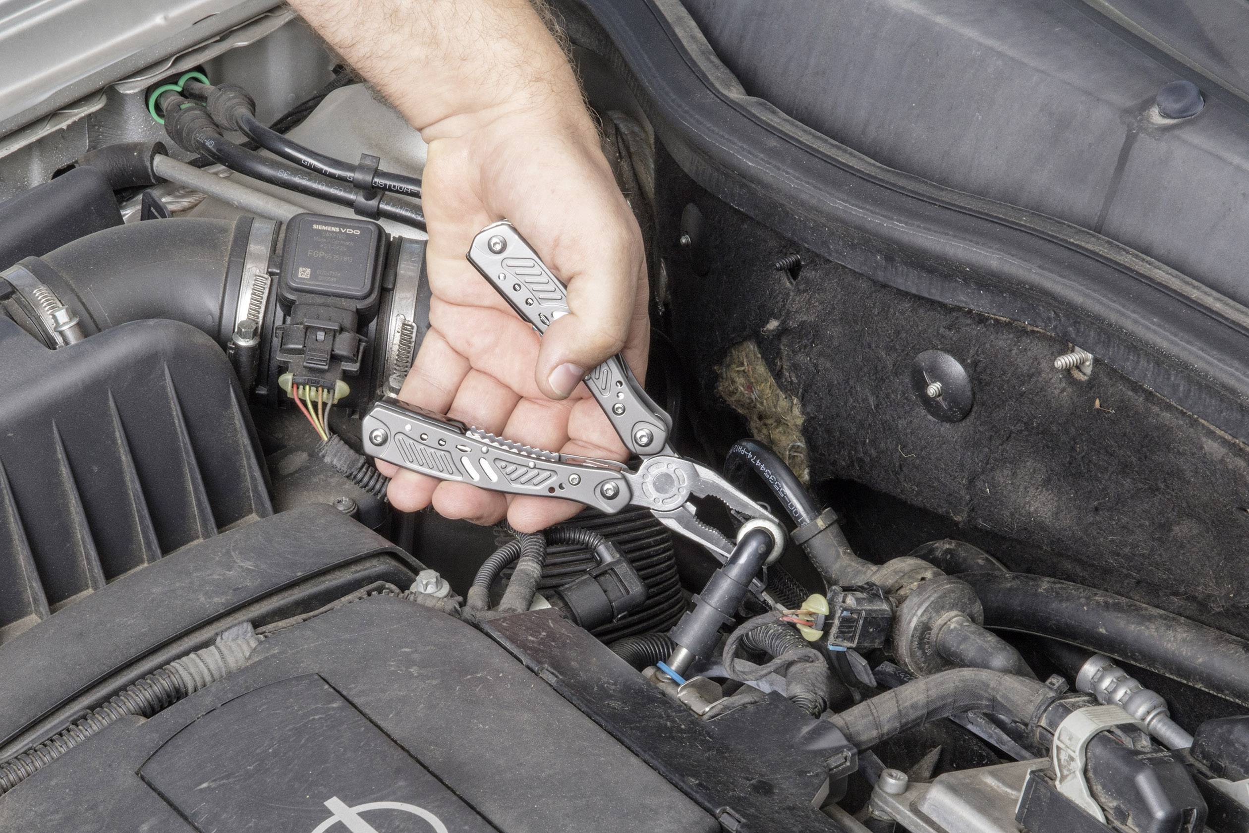 Une personne utilise un outil multifonction pour réparer une partie du moteur d'une voiture. La voiture est ouverte, et l'accent est mis sur l'outil.