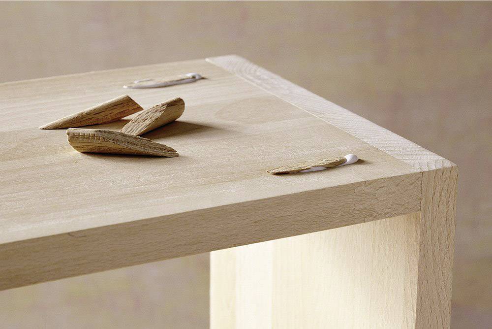 Coin d'une table en bois avec des copeaux de bois et des résidus de colle, probablement lors d'une réparation ou d'un assemblage.