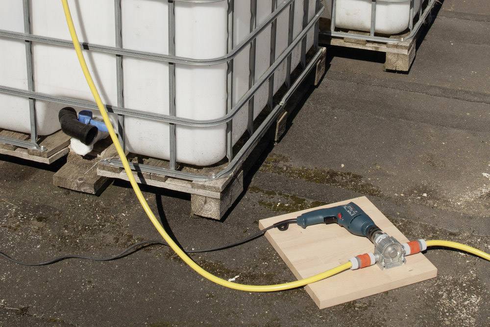 Un grand réservoir d'eau est posé sur une palette. Un tuyau jaune est connecté au réservoir et mène à un appareil électrique placé sur une planche.