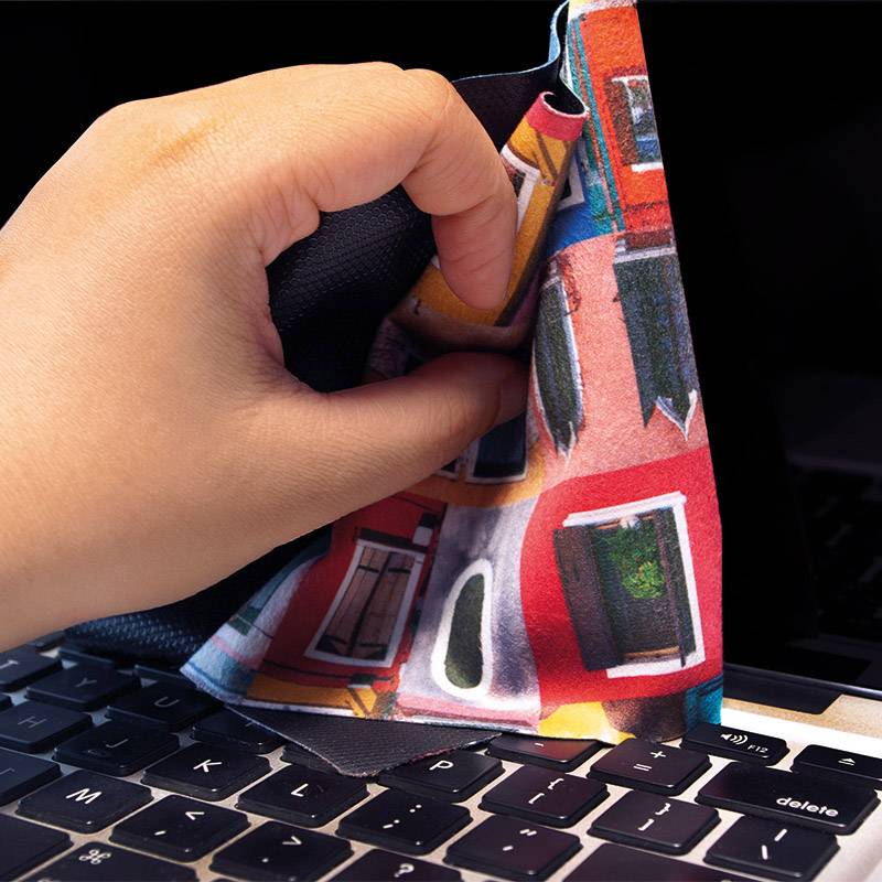 Une main nettoie un clavier d'ordinateur portable avec un chiffon coloré.