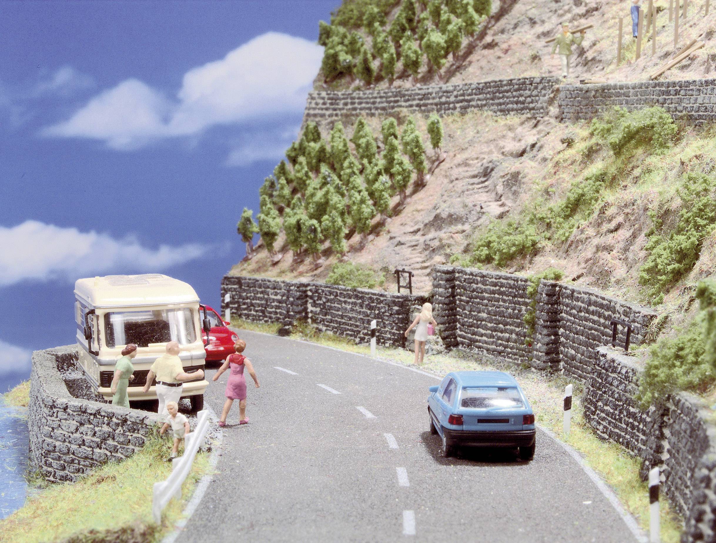 Paysage miniature avec une route sur un flanc de colline, des voitures et des personnes au bord de la route, engagées dans des conversations.