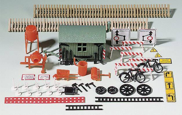 Accessoires de train miniature : Un petit bâtiment vert, des barrières, des panneaux et des vélos pour représenter une scène de chantier.