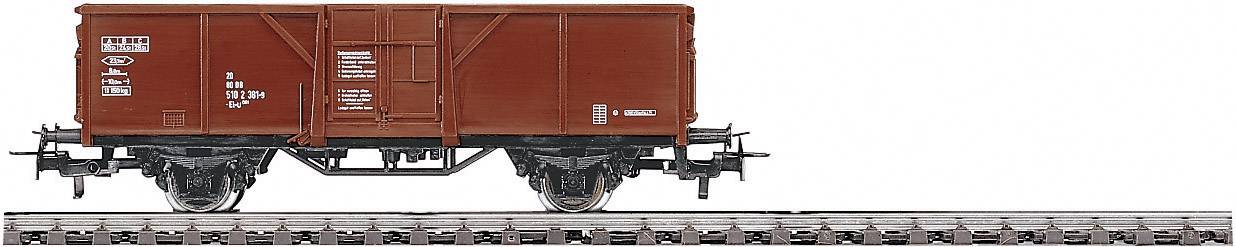 Un wagon de marchandises rouge est stationné sur une section de voie ferrée. Le wagon a une forme rectangulaire et est pourvu de marquages techniques.