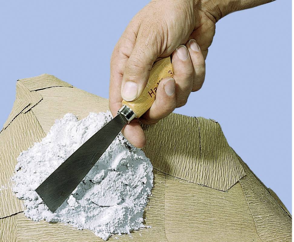 Une main tient un outil à enduire et applique du plâtre blanc sur une surface structurée.