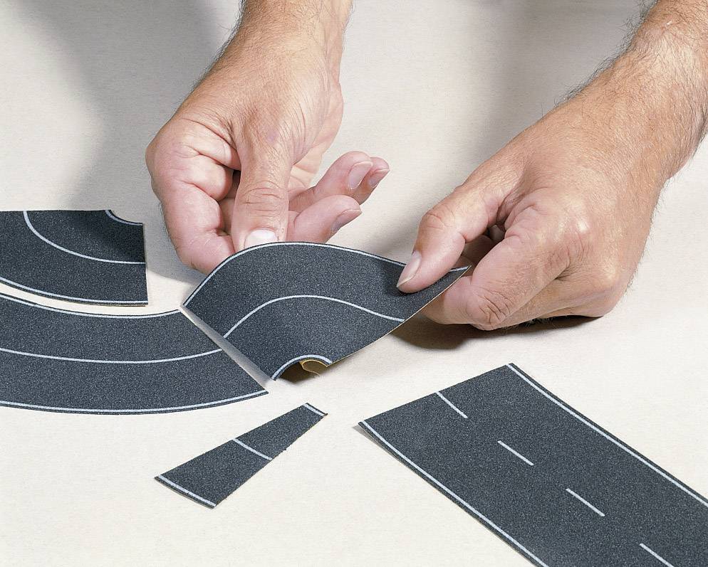 Une personne forme une route à partir de morceaux de papier découpés, avec différentes courbes et directions, sur une table.