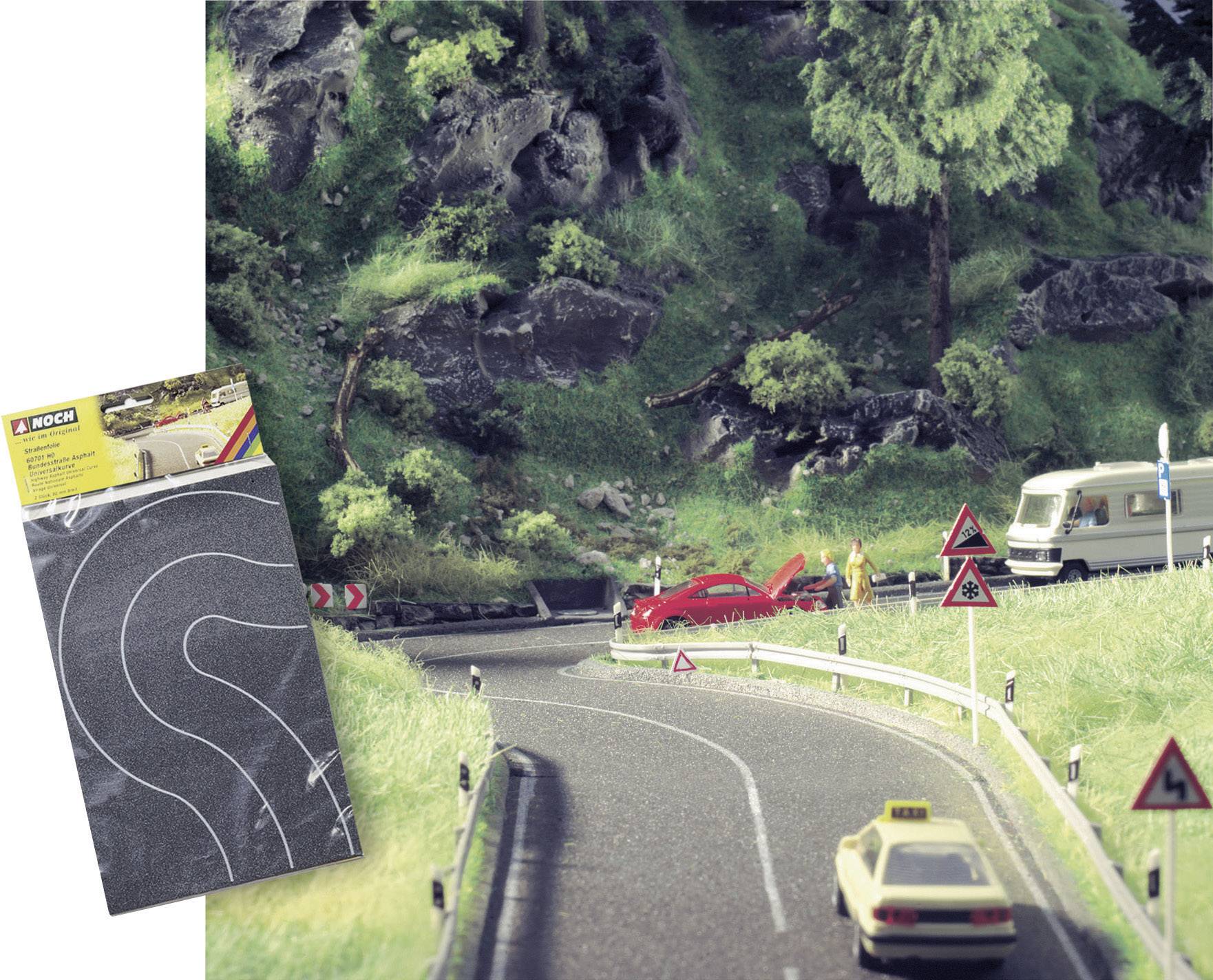 Route modèle avec des virages, une voiture rouge à côté de la route, un camping-car en arrière-plan. Une haie est visible au premier plan.