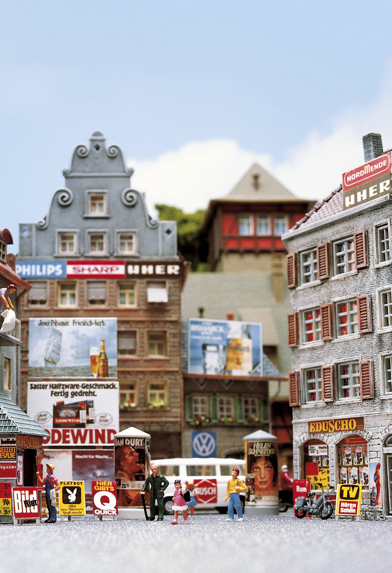 Une scène de ville miniature avec des bâtiments miniatures, des panneaux publicitaires et de petites figurines. Certains bâtiments sont décorés avec des enseignes de marques connues.