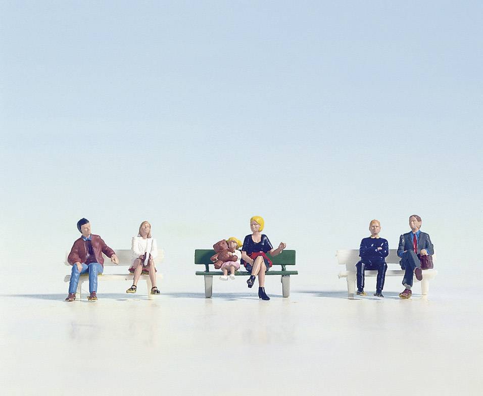 Des figurines miniatures sont assises sur des bancs, distantes les unes des autres, symbolisant la distanciation sociale. Un ciel clair se trouve en arrière-plan.