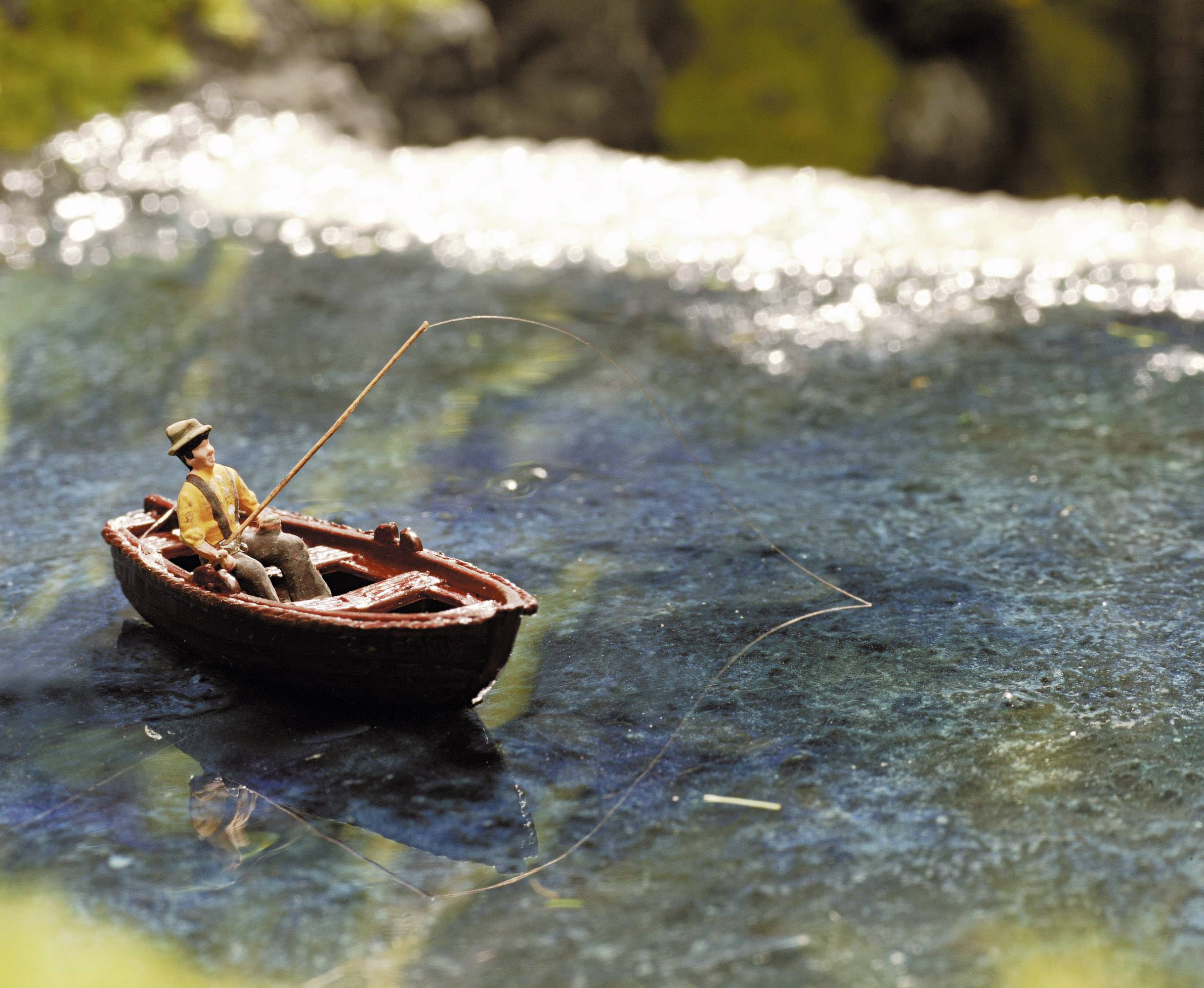 Un homme pêche dans une petite embarcation sur un lac paisible. L'eau est claire et reflète le paysage environnant.