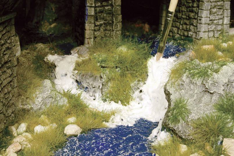 Un modèle d'une scène aquatique avec des pierres, de l'herbe et un petit pont, représente un cours d'eau avec de l'écume blanche, reproduit de manière réaliste.