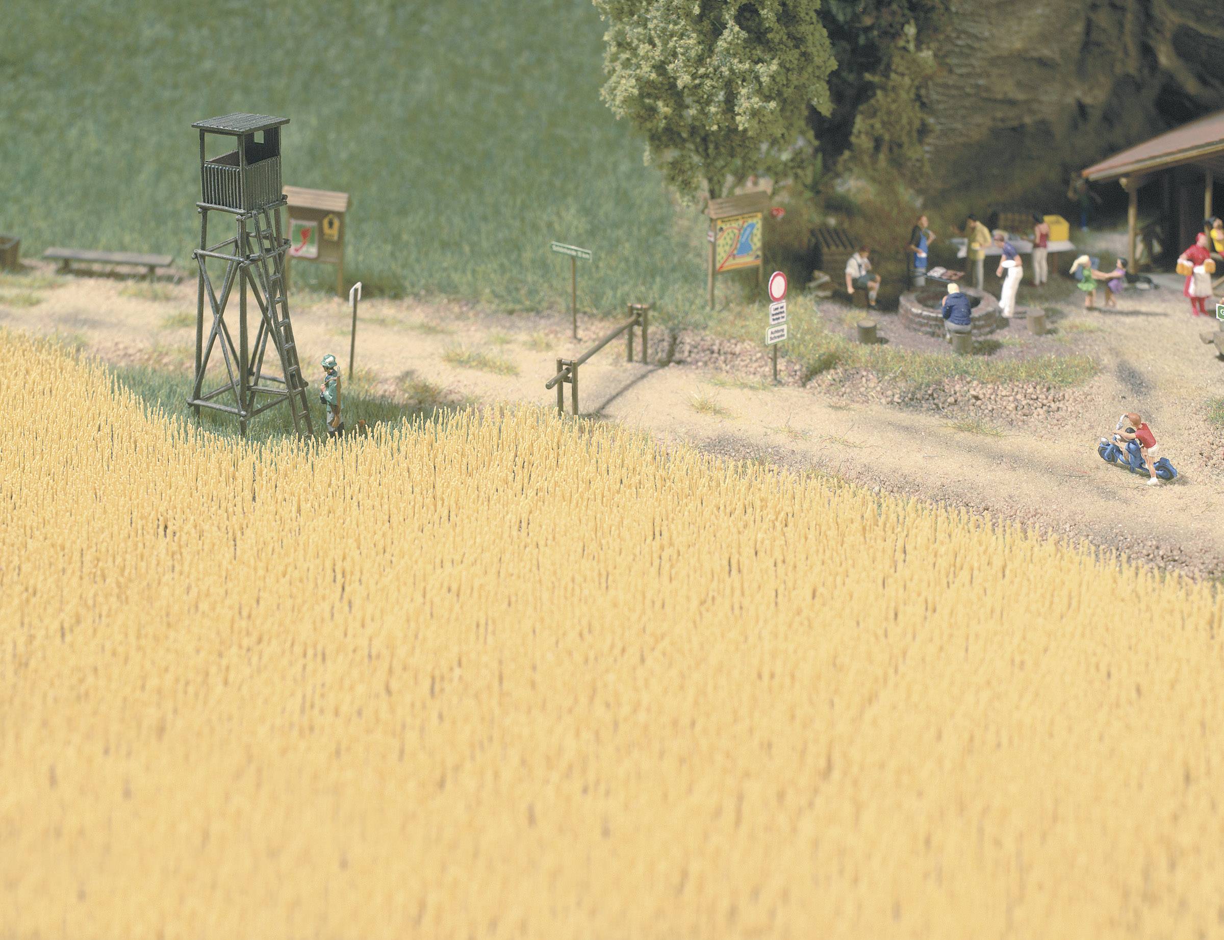 Un modèle miniature représente une scène rurale avec une tour d'observation en bordure d'un champ, un petit groupe de personnes et un bâtiment agricole.