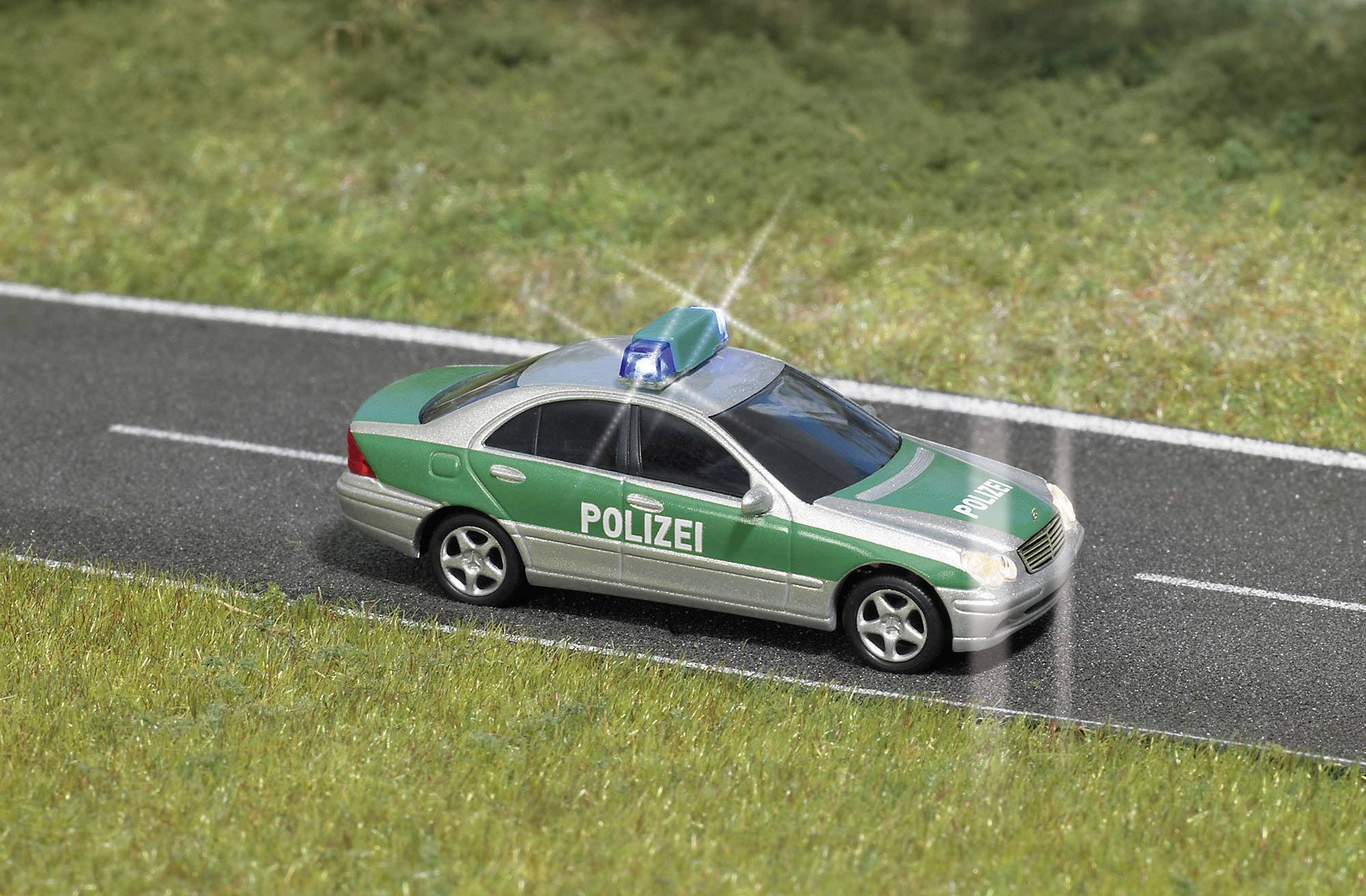 Une voiture de police verte avec des gyrophares bleus sur une route, entourée d'herbe ; illustrant la présence policière dans un environnement rural.