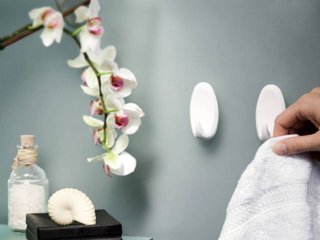 Une main accroche une serviette à un crochet blanc. À côté, une orchidée, un verre de sel de bain et un coquillage.