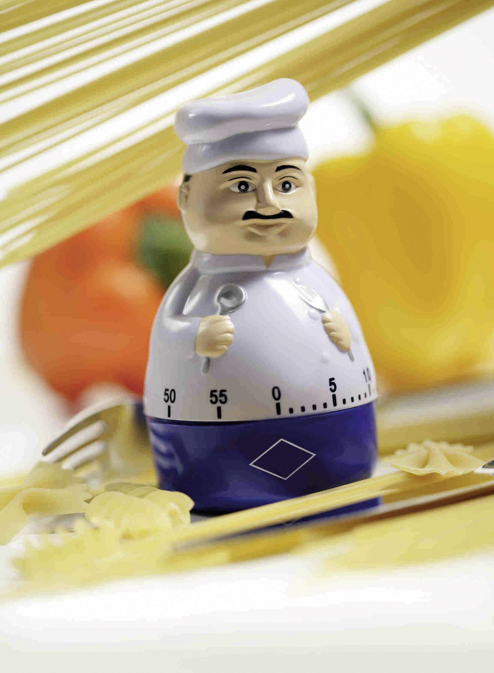 Un minuteur de cuisine en forme de chef cuisinier, entouré de pâtes, d'une fourchette et de poivrons dans le fond.