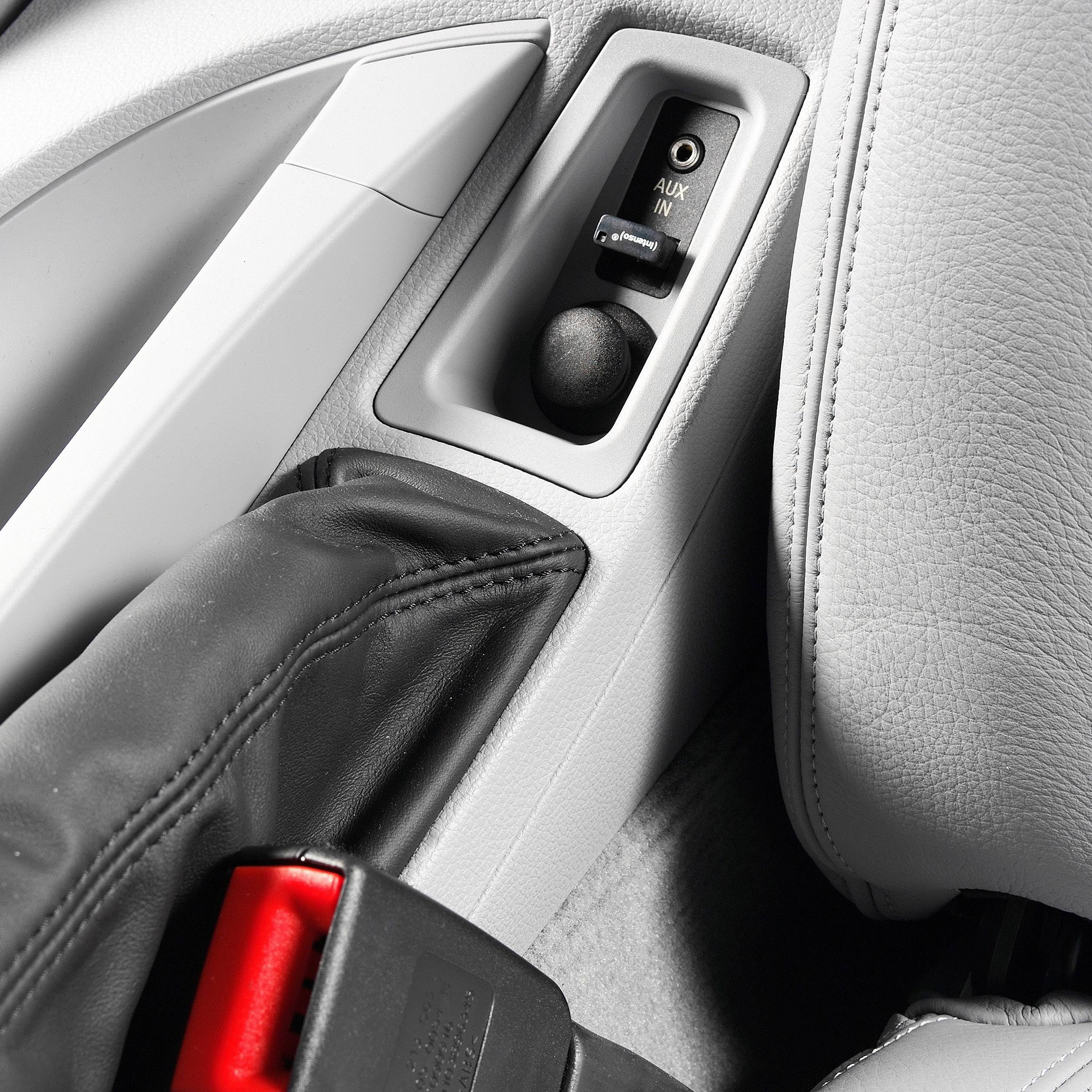 L'intérieur de la voiture montre une entrée AUX et une ceinture de sécurité rayée rouge et noire.