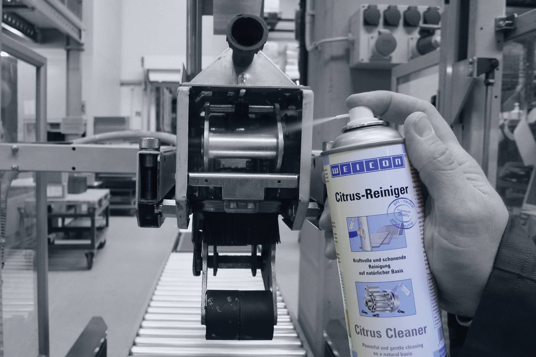 Une main vaporise un aérosol de nettoyant 'Citrus' sur une pièce métallique dans un environnement industriel. Processus de nettoyage dans un hall d'usine.