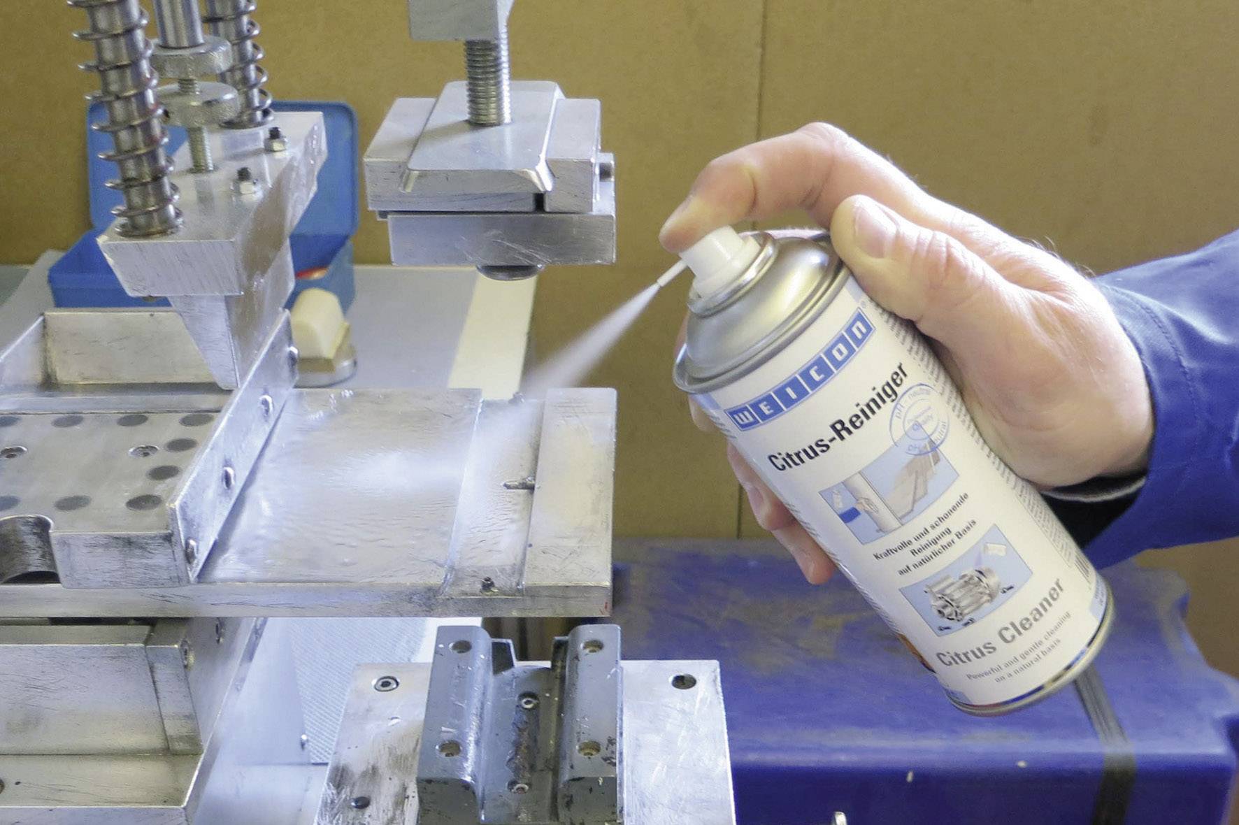 Une personne pulvérise un produit à partir d'un aérosol sur une surface métallique de machine. L'aérosol est étiqueté comme un 