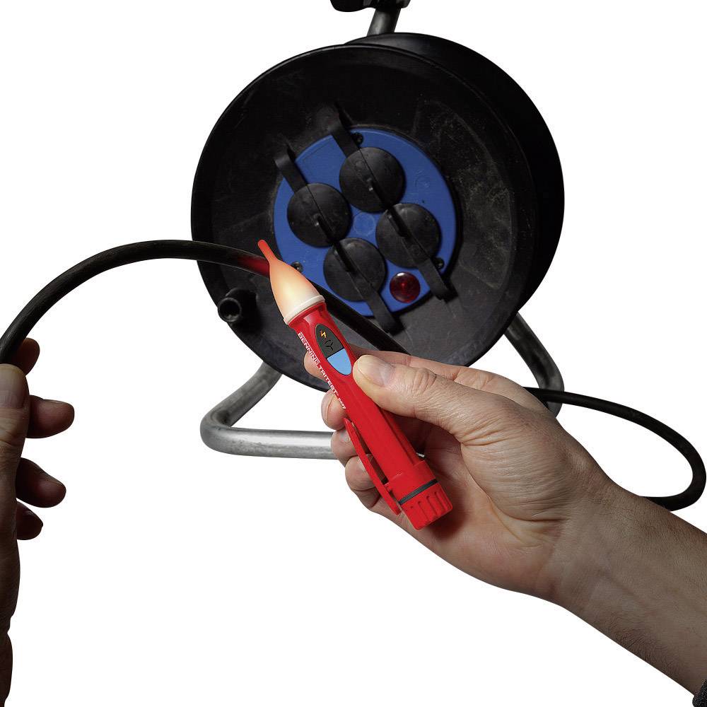Une personne teste un câble noir à l'aide d'un testeur de tension rouge, provenant d'un touret de câble, afin de vérifier la présence de courant électrique.