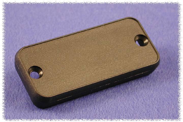 Un composant rectangulaire, noir et plat avec deux trous, posé sur un fond lilas.