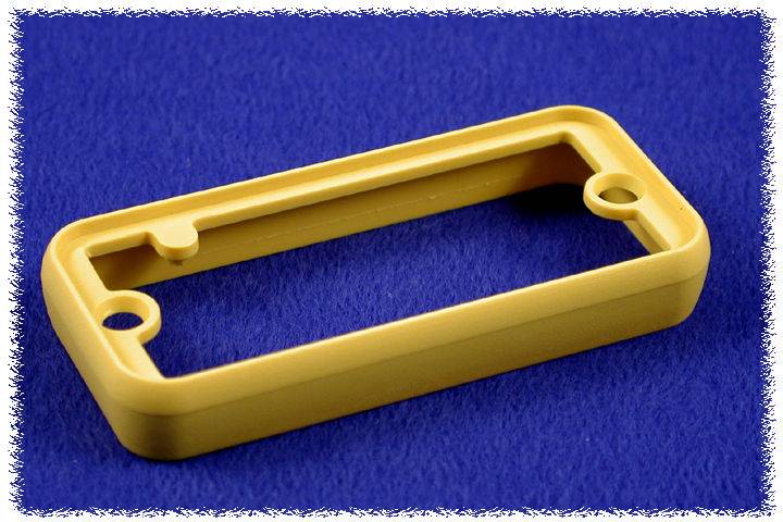 Pièce rectangulaire jaune en plastique avec deux trous, posée sur un fond bleu.