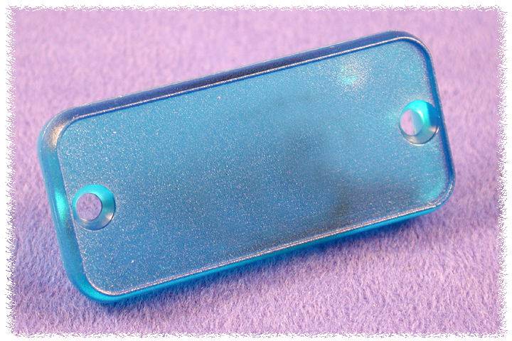 Couverture rectangulaire en plastique bleu transparent avec des coins arrondis et deux trous de vis sur les côtés, sur un fond violet.