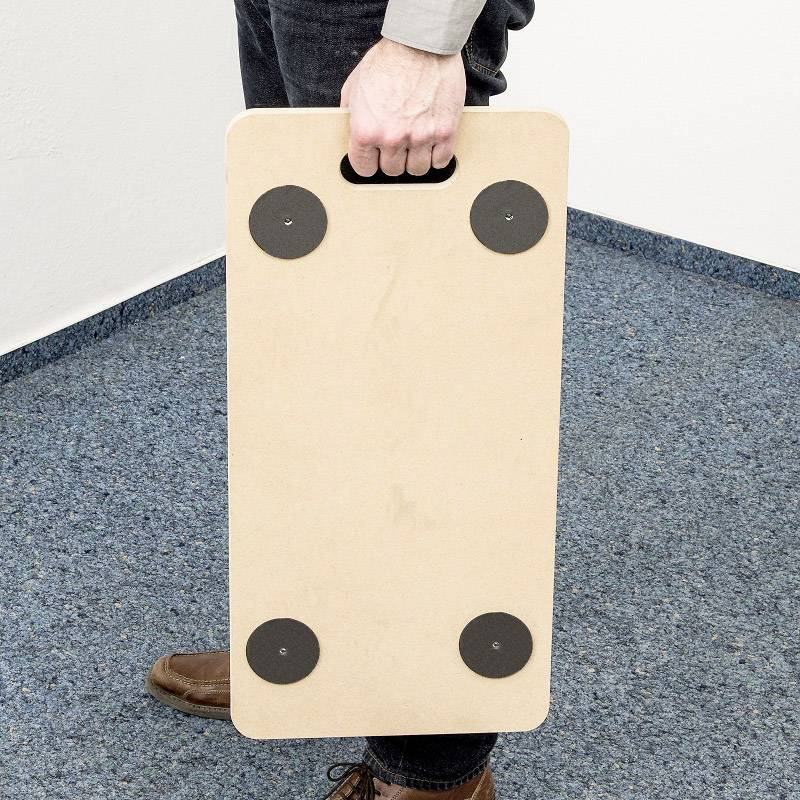 Une personne tient une planche rectangulaire en bois avec quatre surfaces de glissement rondes noires sur un tapis bleu.