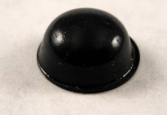Un objet noir, hémisphérique, posé sur une surface claire, probablement un patin de meuble ou un embout en caoutchouc.