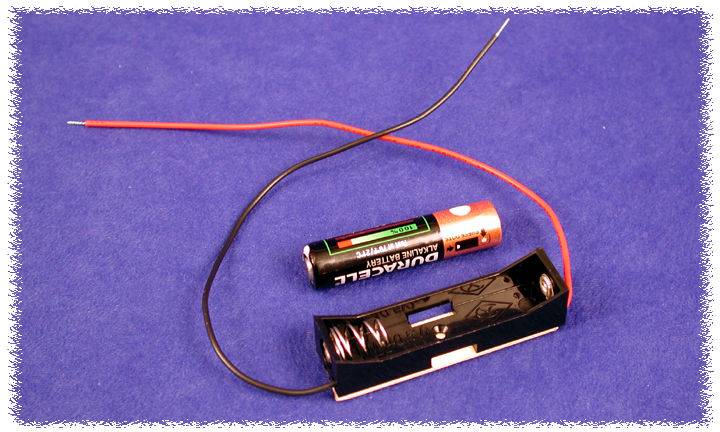 Une pile AA est posée à côté d'un support de batterie noir avec deux fils, sur un fond bleu.
