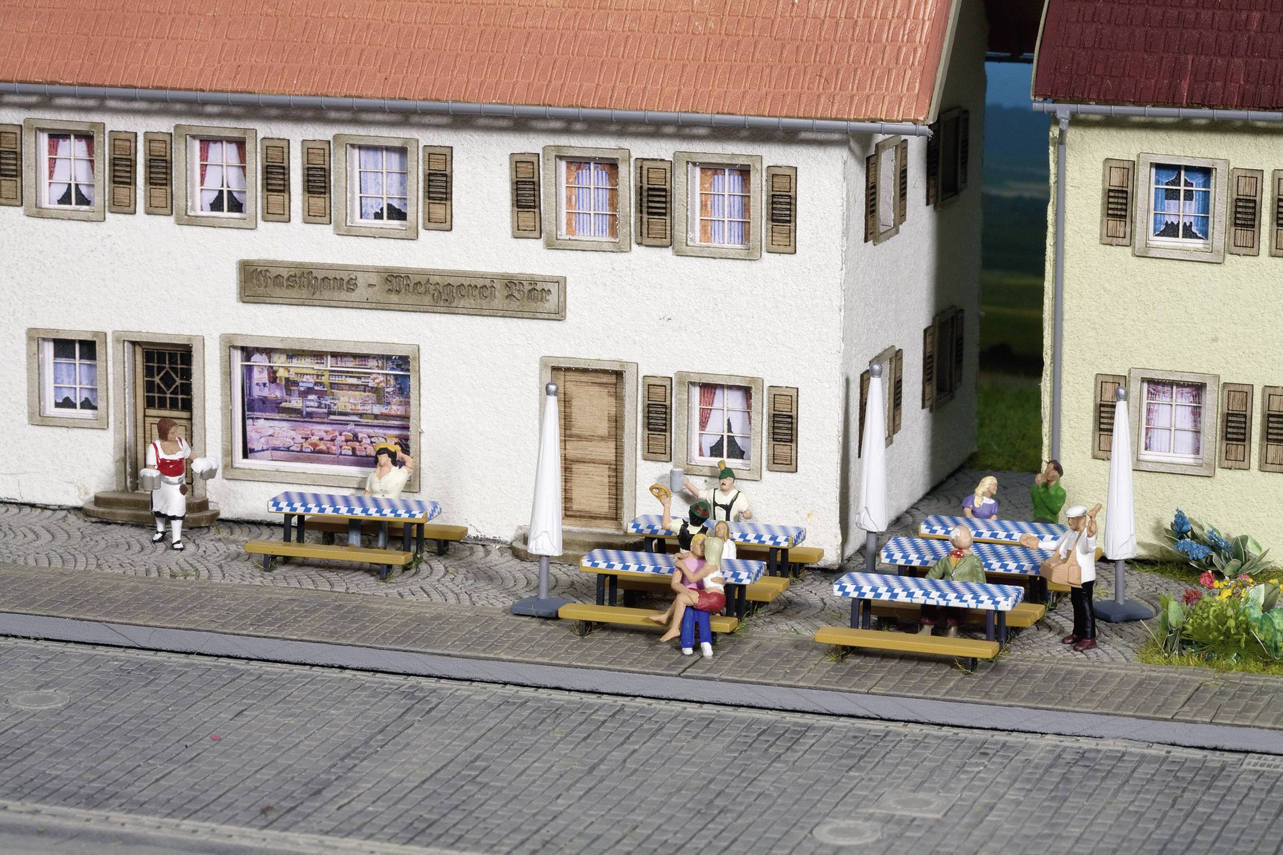 Modèle miniature d'une scène de rue avec des bâtiments, des personnages et des tables représentant un café. Des personnes sont assises à des tables à carreaux bleu et blanc.