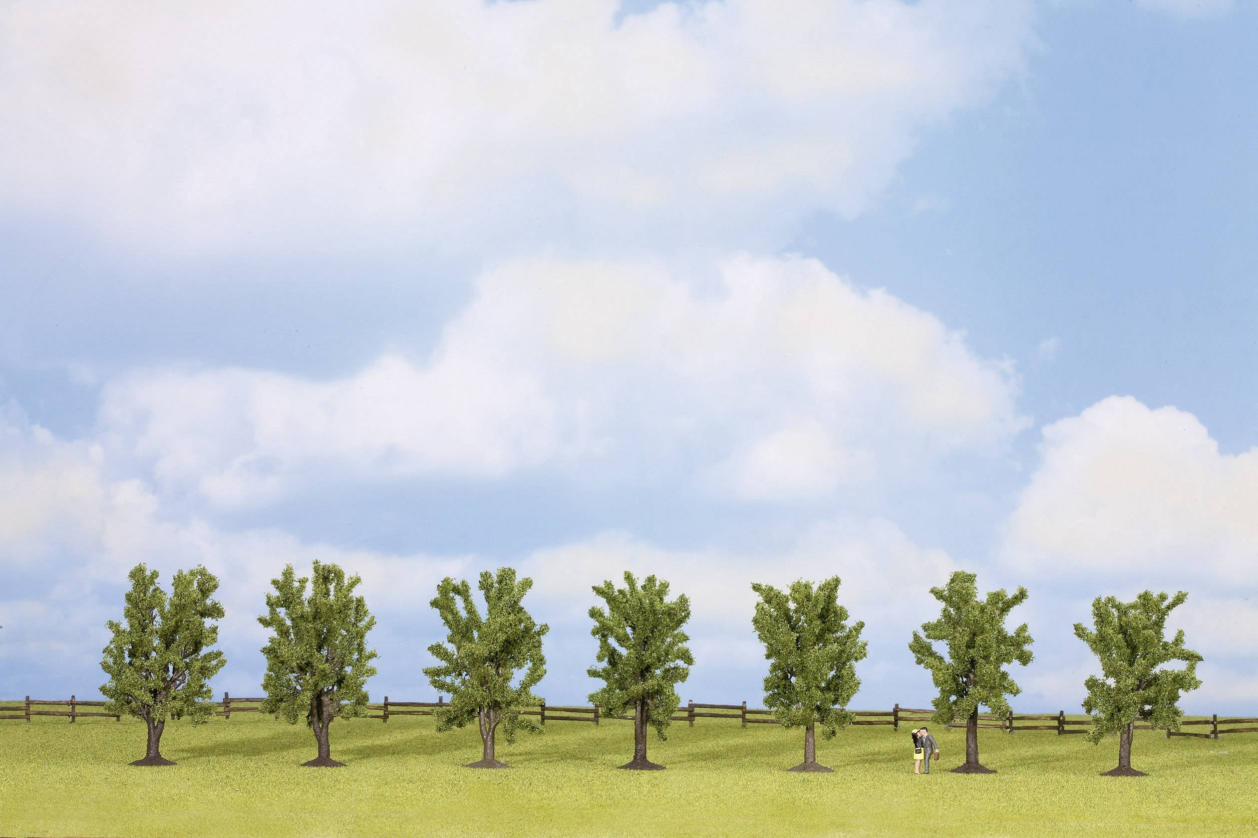 Une rangée de sept arbres se dresse sur une prairie verte sous un ciel bleu parsemé de nuages. Une minuscule silhouette examine quelque chose.
