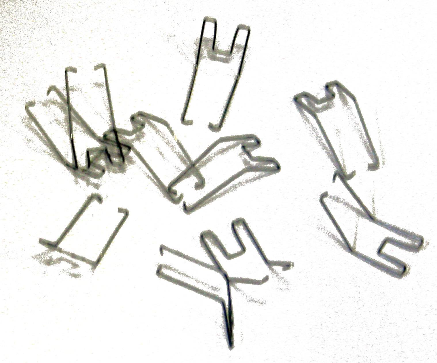 Agrafes métalliques dispersées sur une surface blanche. Les agrafes sont en forme de U et servent à fixer des câbles.