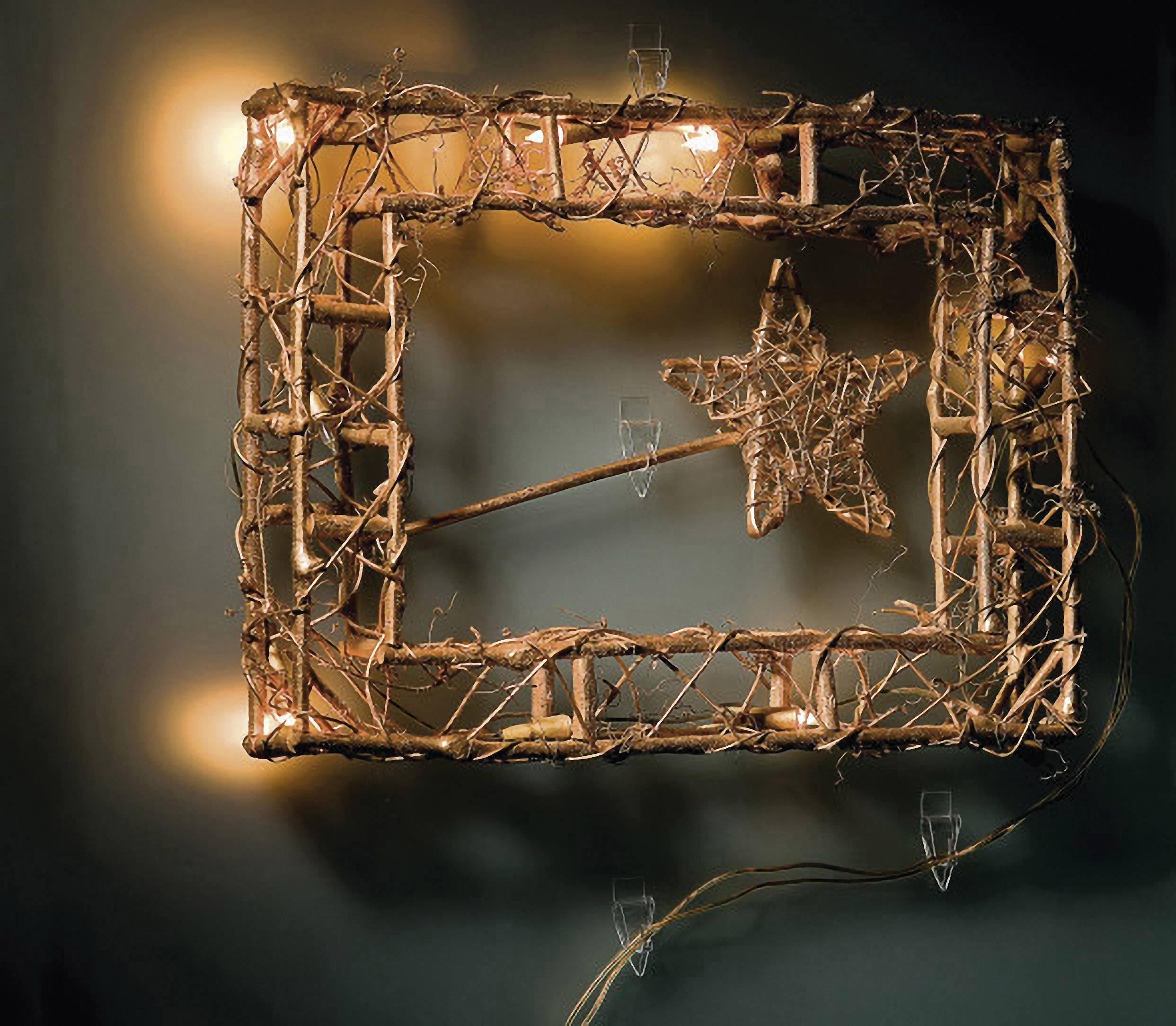 Un cadre en bois rectangulaire et lumineux, portant une étoile faite de branches, suspendu à un mur sombre.