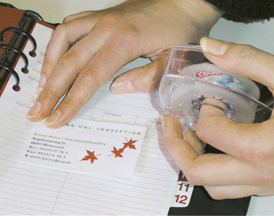 Une personne utilise du ruban adhésif pour coller une carte de visite dans un carnet de notes. La carte comporte des étoiles rouges et des informations de contact.