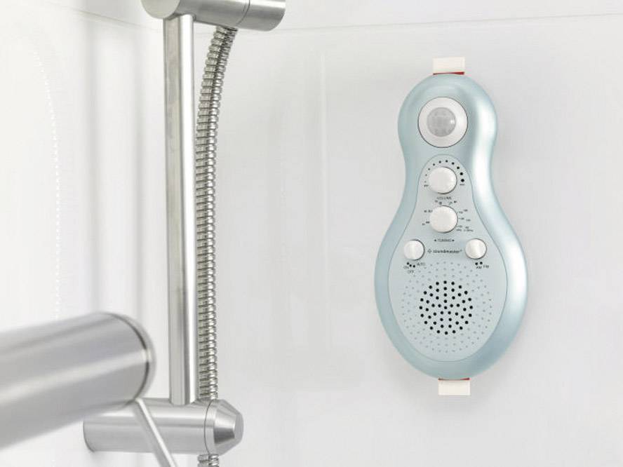 Un radio de douche bleu est fixé sur un mur de salle de bain blanc à côté d'un pommeau de douche. Il dispose de trois boutons et d'un haut-parleur.