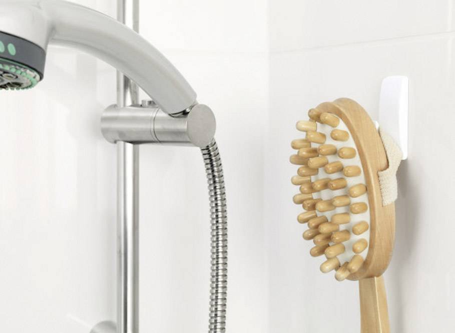 Une pomme de douche et une brosse de baignoire en bois sont suspendues côte à côte sur un mur de salle de bain.