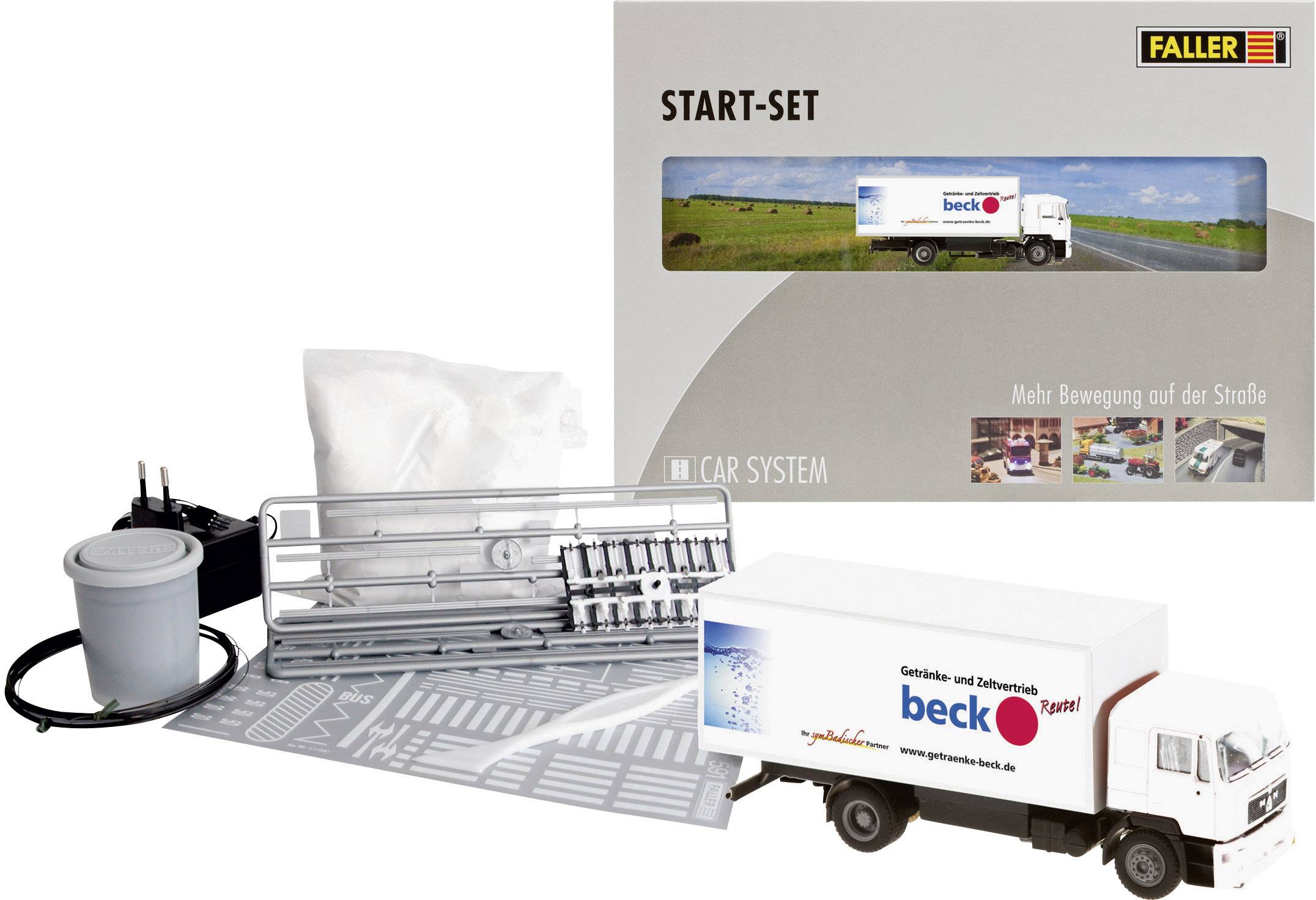 Coffret de départ pour train miniature avec modèle de camion, éléments de décoration et accessoires. L'emballage présente un paysage et un camion sur une route.