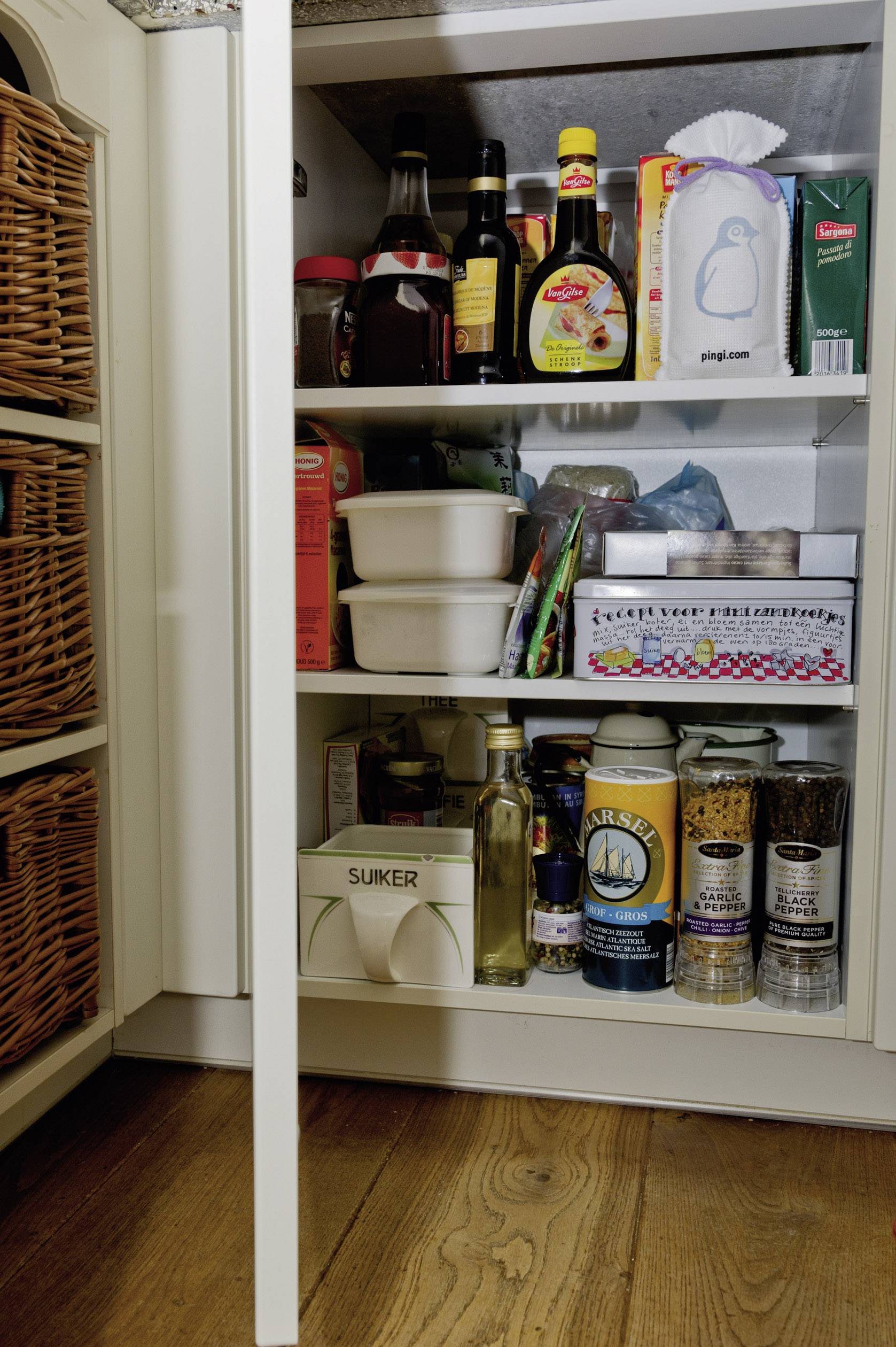 Coup d'œil dans le garde-manger : étagères garnies de denrées alimentaires telles que des épices, du sucre, des bouteilles de sauce et des aliments emballés.