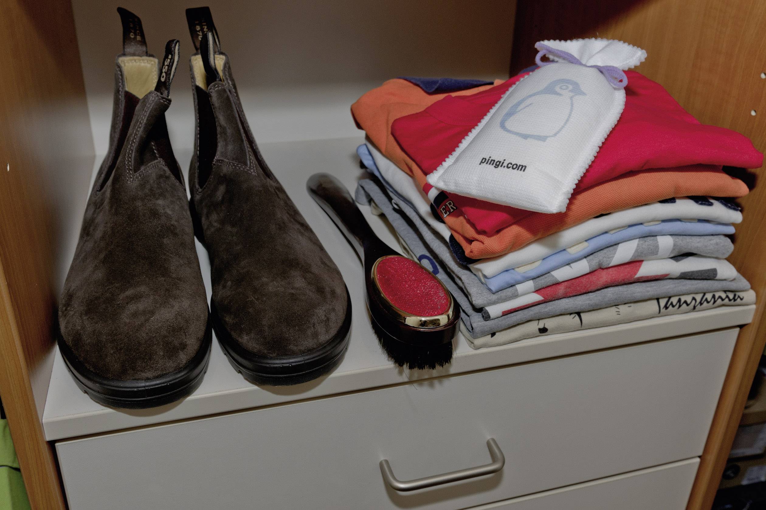 Une paire de chaussures brunes, une brosse à vêtements et une pile de t-shirts colorés pliés sont soigneusement rangés sur une étagère.