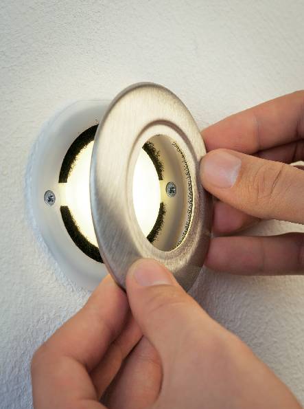 Une personne utilise ses deux mains pour ouvrir ou fermer un couvercle de ventilation rond installé dans un mur.