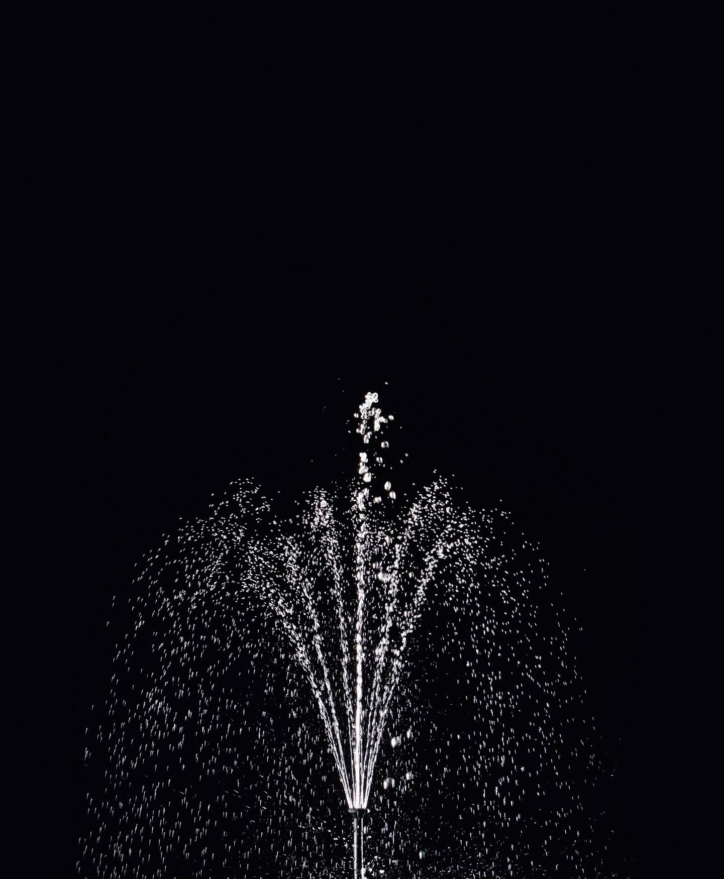 Une fontaine d'eau jaillit dans la nuit sur un fond noir.