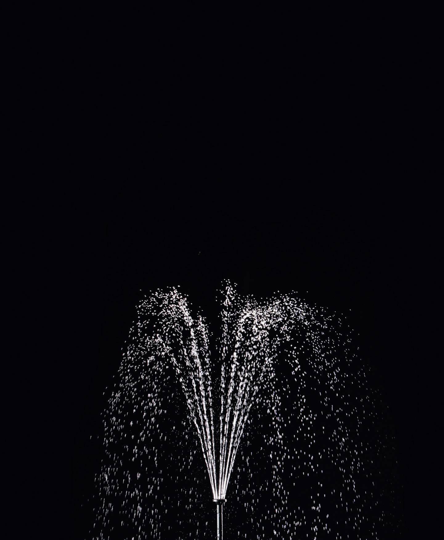 Une fontaine propulse de l'eau dans les airs devant un fond sombre, mettant en valeur les gouttelettes d'eau grâce à la lumière.